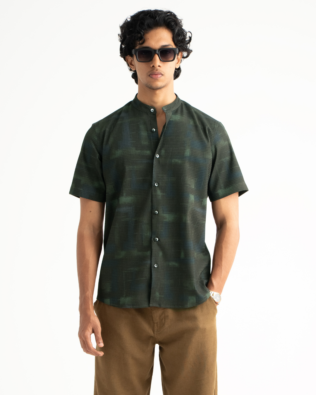 Man wearing a green patterned shirt and sunglasses on a white background